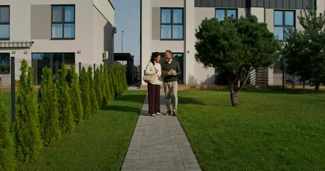 A man and a woman study the design project of a house while walking in the backyard. Making a decision about buying a property