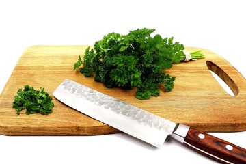Fresh bunch and sliced ​​curly parsley lie on a wooden board with cutting knife isolated on a white background.