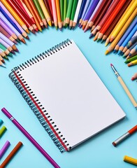Fototapeta premium Blank spiral notebook surrounded by colorful pencils arranged neatly on a white background, ready for drawing or sketching