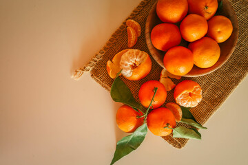 Fresh juicy tangerines with green leaves placed on a rustic burlap cloth, illuminated by warm...