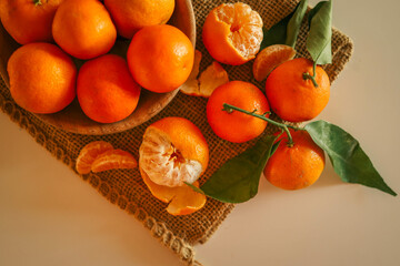 Fresh juicy tangerines with green leaves placed on a rustic burlap cloth, illuminated by warm...