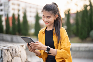 Smiling young Asian woman using digital tablet in urban city