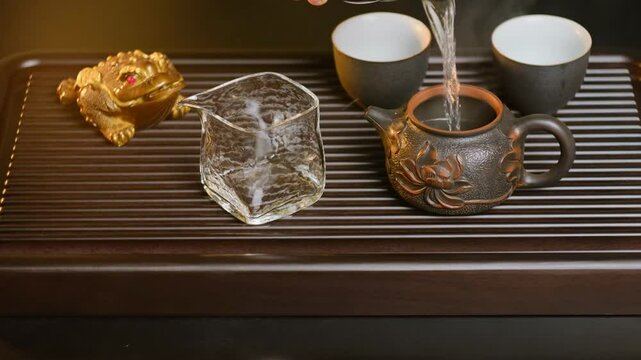 Chinese tea ceremony close-up showing water being poured into an intricately designed teapot alongside a golden money toad figurine and traditional teaware.