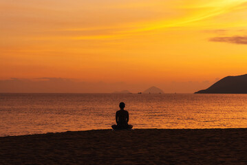 The silhouette of a man sitting on the beach at dawn