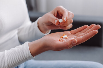 Close up of female hand holding pills sitting on couch, painkiller medicine from stomach pain,...