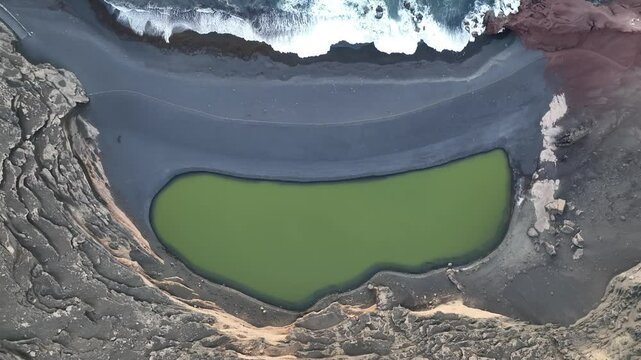 Aerial view of a serene green lake surrounded by rugged cliffs and a beautiful coastline, Yaiza, Spain.