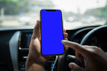 Hand holding white mobile phone with blank blue screen in car.