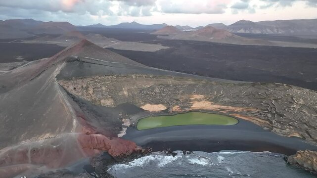 Aerial view of a green lake surrounded by a volcanic landscape with rugged mountains and ocean, Yaiza, Spain.