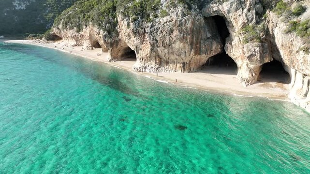 Aerial view of grottoes and cliffs with turquoise water and sandy beach, Dorgali, Italy.