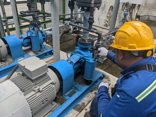 A technician is inspecting an industrial pump, wearing safety gear and checking the equipment.
