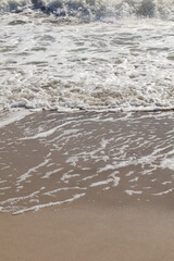 Close-up of delicate foam patterns left on the sandy shoreline as ocean waves recede, creating a serene and textured coastal scene