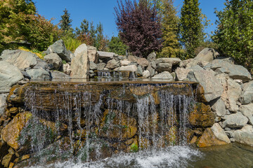 Water falls from height of 7 meters into artificial rocky riverbed. Close-up. Triple waterfall in...