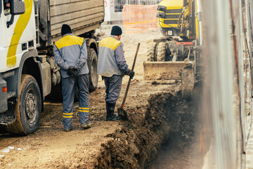 Construction workers repairing a burst water pipe under winter conditions. Excavator and truck on a...