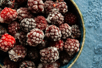 Frozen blackberries glistening in a bowl, set against a striking dark blue backdrop.