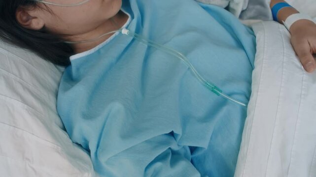 Tilt shot of sleeping Caucasian girl with nasal cannula lying in hospital bed with intravenous injection in median cubital vein during recovery period in clinic