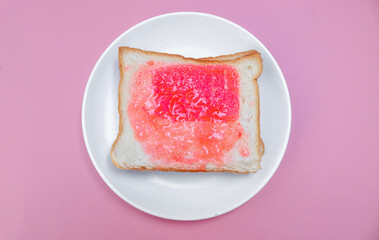 close up of white toast bread with strawberry jam on a plate, two sliced ​​bread isolated on pink background. Simple breakfast Toast with jam