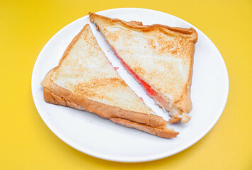 close up of white toast bread with strawberry jam on a plate, two sliced ​​bread isolated on yellow background. Simple breakfast Toast with jam