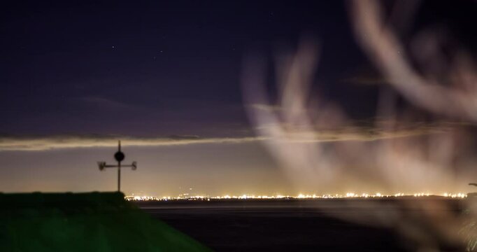 Time Lapse with moving clouds in the evening with a weather vane in the foreground, over Flase Bay Harbor, Cape Town, South Africa