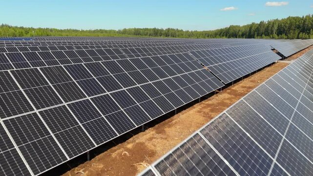 Aerial low fast dolly pullback over top of bifacial panels at Solar Farm showcasing renewable energy production in forest