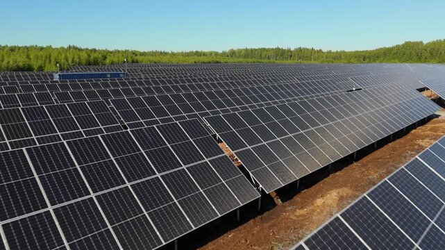 Low angle aerial dolly over top of bifacial solar panels at Solar Farm, Finland, with clear skies over green forest