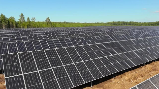Aerial orbit and rise over Solar Farm in Finland showcasing renewable energy and bifacial panels sweeping out to forest tree line