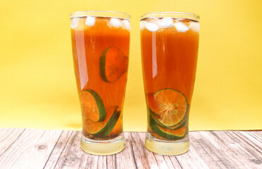 Close up Glass of iced tea with lemon, lime and ice cubes isolated on yellow background and table. Two glasses of sweet iced tea filled with lemon slices