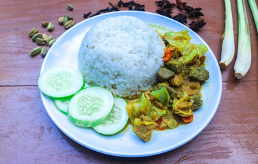 Beef tongseng with curry sauce, with vegetables served with rice in a white plate and garnished with spices. Beef tongseng contains pieces of cabbage, cayenne pepper, tomatoes.