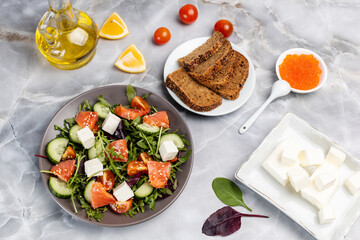 Salad with salmon, white cheese and vegetables on the plate with ingredients.