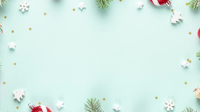 Christmas frame made of snowy fir branches, red decorations, gift boxes, candy and pine cones on pastel blue background. Flat lay. Happy New Year and winter holidays background. Top view