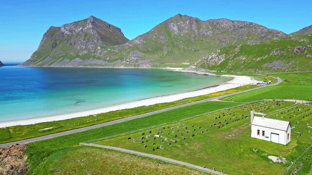 Aerial view of Haukland beach and bay with a scenic chapel and serene mountains, Leknes, Norway.