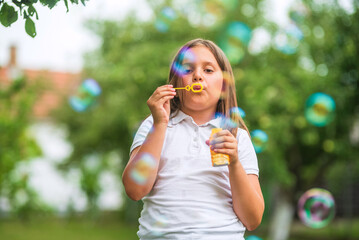 Young girl blowing soap bubbles in summer park