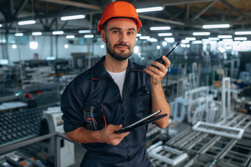 Giving instructions, using radio, walkie talkie. Man is working in the modern factory