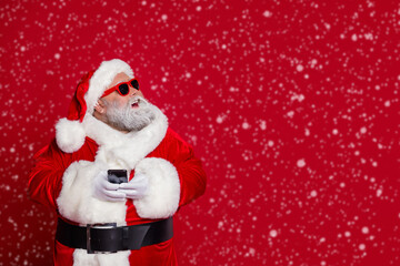 Photo of dreamy old man hold telephone look empty space wear santa hat costume isolated red color background