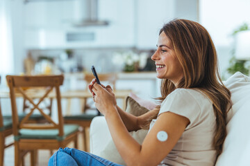Smiling Woman Using Smartphone With Diabetes Monitor at Home