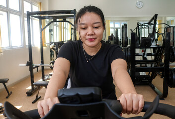 Front view of smiling young woman in sportswear riding on a stationary bike at the gym. Work out for beginners