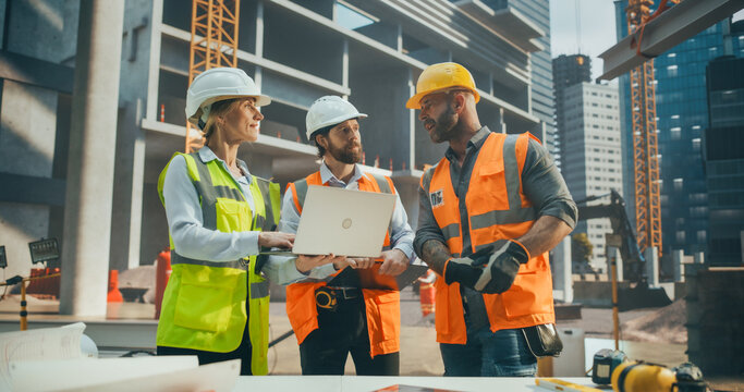 Portrait of a Site Manager Talking with General Operatives at a Residential Building Construction Area. Female and Male Employees Using a Laptop Computer to Oversee the Real Estate Project Plan