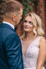 Obraz premium beautiful blonde bride looks at the groom smiling at her in front of the ivy wall
