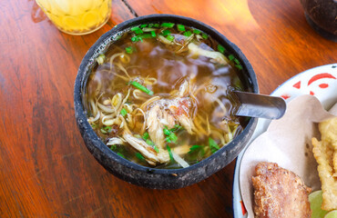 Soto Ayam and beef soto in coconut shell bowls on wooden table with mendoan snacks, satay and drinks. Traditional Indonesian soup mainly consists of broth, meat or chicken, and vegetables.
