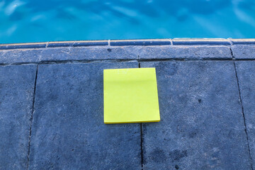 blank yellow sticky note paper on the floor with swimming pool and blue water background. Blank space for text