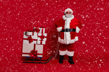 Photo of cheerful reliable old man prepare gift sleigh delivery wear santa hat costume isolated red color background