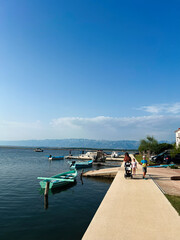 Serene lakeside promenade with family strolling under clear blue sky. Nin, Croatia.