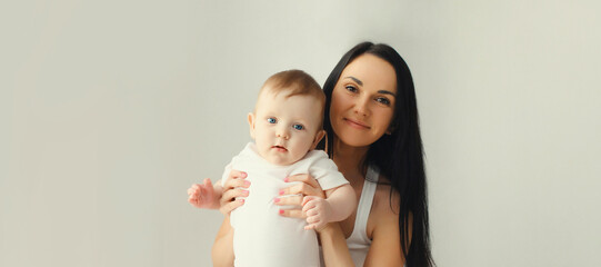 Happy smiling young mother playing with baby in white room at home