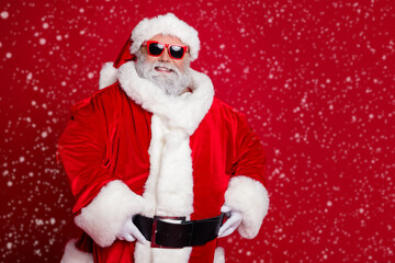 Photo of cheerful positive confident retired man hands belt wear santa hat costume isolated red color background