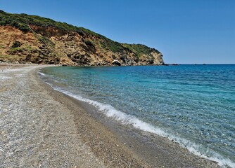 Obraz premium Pebble turquoise beach of Xanemos, above which planes take off and land. Greek island of Skiathos, Europe.