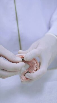 Dental prosthesis in the hands of the doctor close-up. Dentist holding ceramic dental bridge. Front view of complete denture. Dentistry conceptual photo. Prosthetic dentistry. False teeth