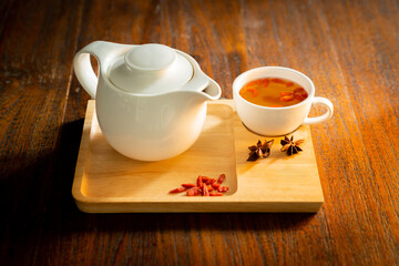 White tea set of cups and teapot featuring goji berries and two star anise pods on a wooden tray with copy space, a tea set on wooden background
