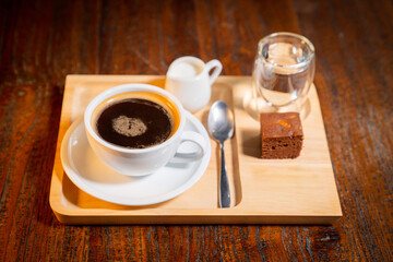 Wooden tray with copy space featuring a cup of coffee, a small cream pitcher, a glass with water, a...
