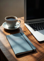 a cup of coffee next to an opened laptop and a blue notebook on a wooden table