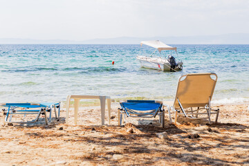 Relaxing Beach Scene With Sun Loungers Facing Clear Blue Sea And Anchored Boat