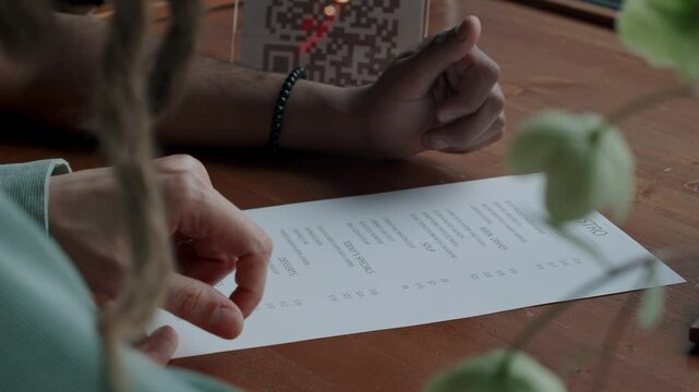 Close-up shot of two unrecognizable people looking through menu at restaurant, suggesting dishes with their fingers